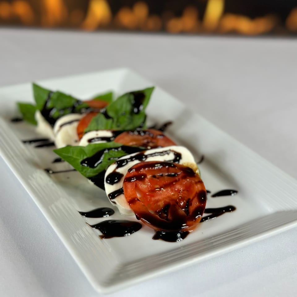 Caprese salad with tomatoes, mozzarella, basil, and balsamic glaze on a white rectangular plate.