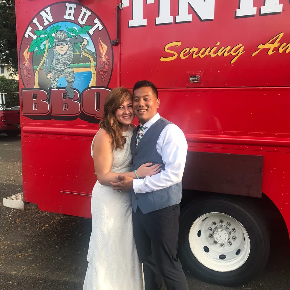 Couple embraces in front of a bright red Tin Hut BBQ food truck.