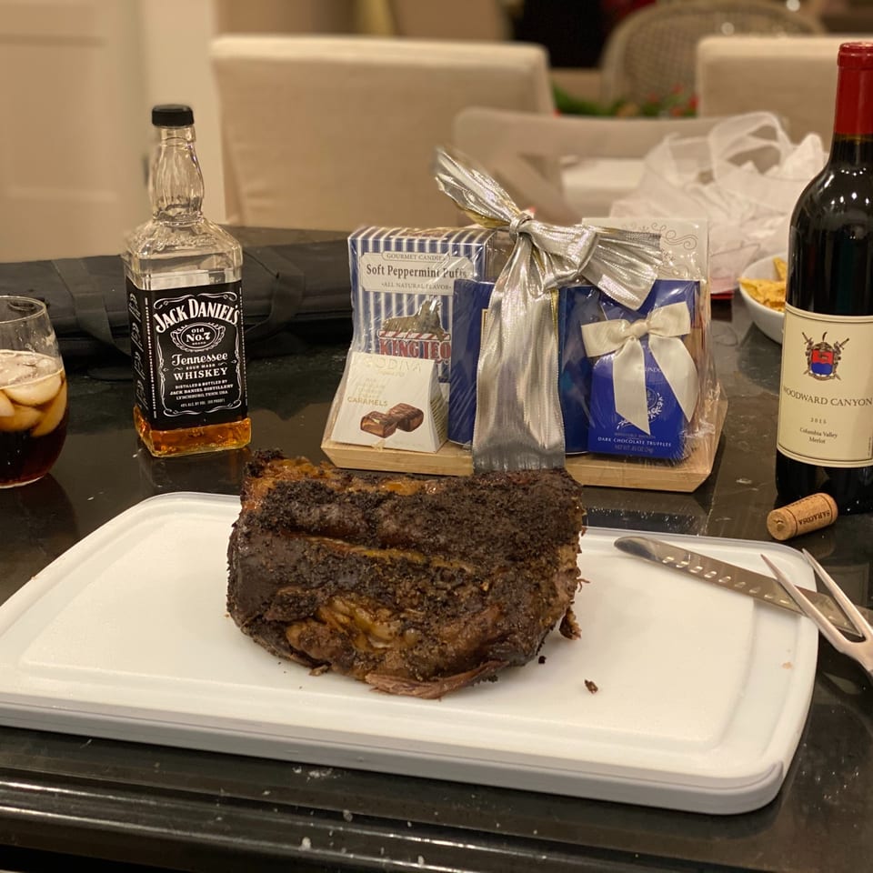 Sliced roast rests on a serving platter beside whiskey, red wine, a gift basket, and dining utensils.