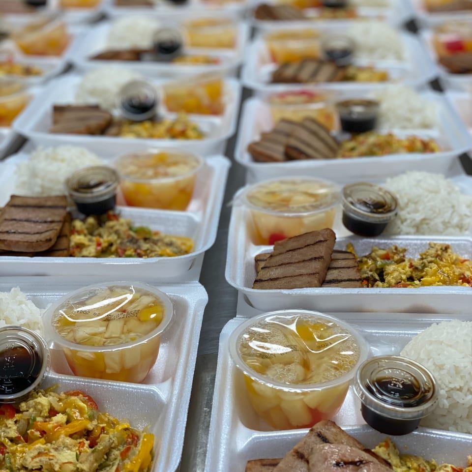 Rows of takeout containers filled with rice, grilled meat, scrambled vegetables, fruit cups, and small sauce containers.