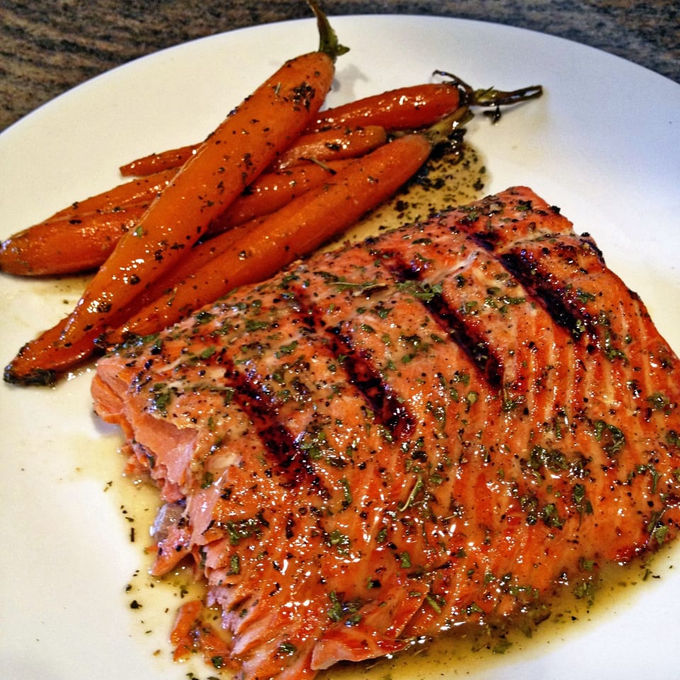 Herb-seasoned grilled salmon fillet served with glazed roasted carrots on a white plate.