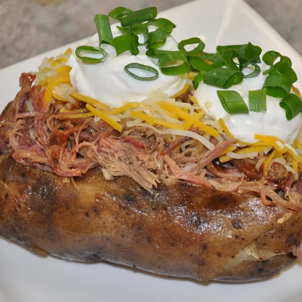 A Tin Hut BBQ baked potato loaded with pulled pork, shredded cheese, sour cream, and green onions.