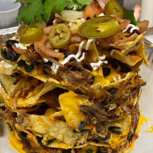 Towering Tin Hut BBQ nachos with pulled pork, cheese, black beans, jalapeños, and cilantro.