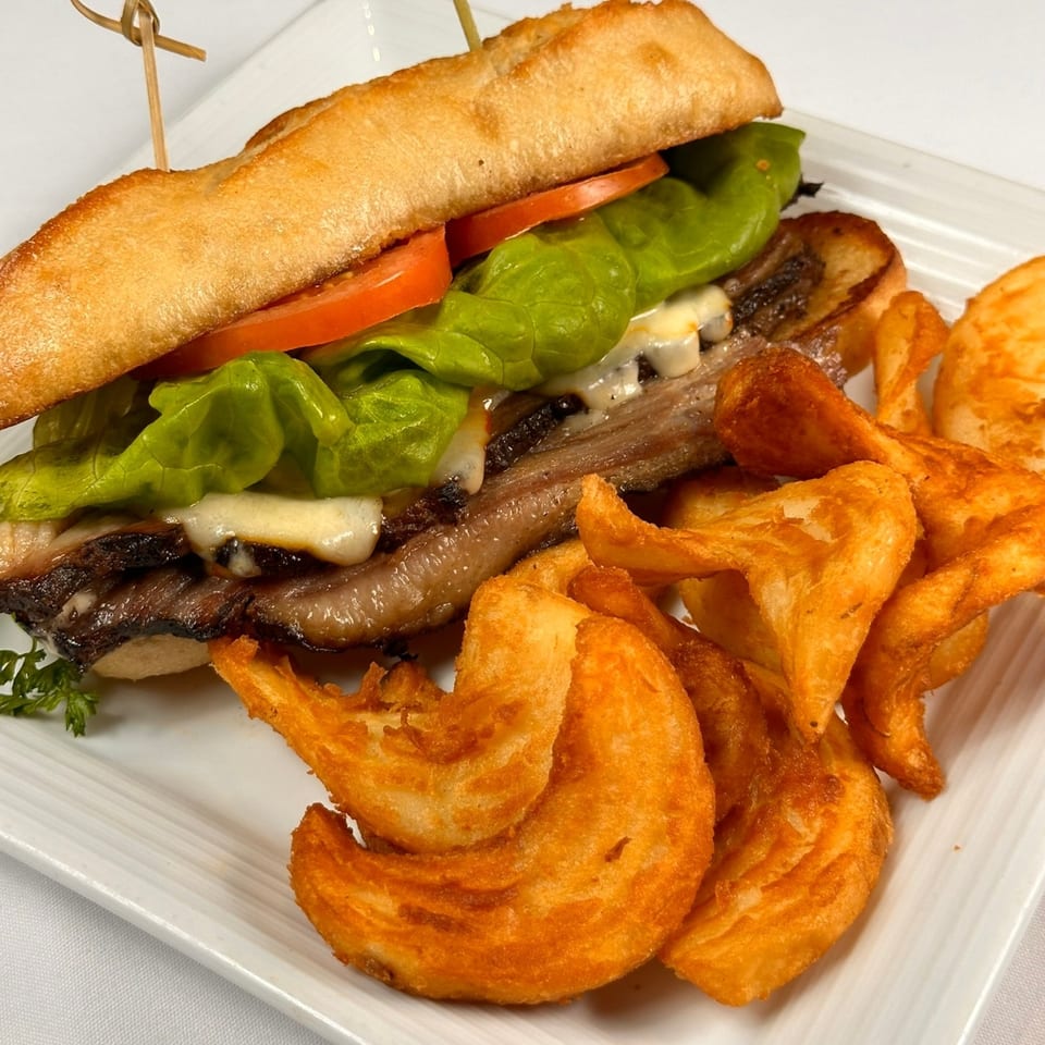 Tin Hut BBQ's brisket sandwich with melted cheese, lettuce, tomato, and curly fries on a white plate.